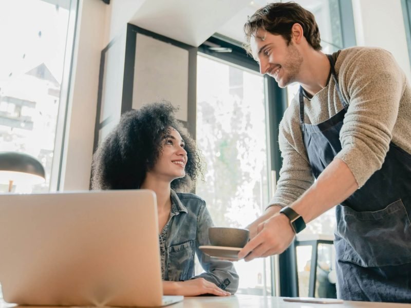young-handsome-waiter-servicing-black-girl-customer-with-laptop-in-cafe.jpg